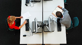 Das Bild zeigt einige Computerarbeitspl?tze von oben. An einem Computer sitzt eine bwin_bwinֹӭ@. An einem anderen Computer sitzt ein Student.