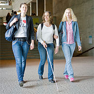 Eine sehbehinderte bwin_bwinֹӭ@ mit Blindenstock wird von zwei sehenden bwin_bwinֹӭ@nen durch das Zentrale H?rsaalgeb?ude begleitet